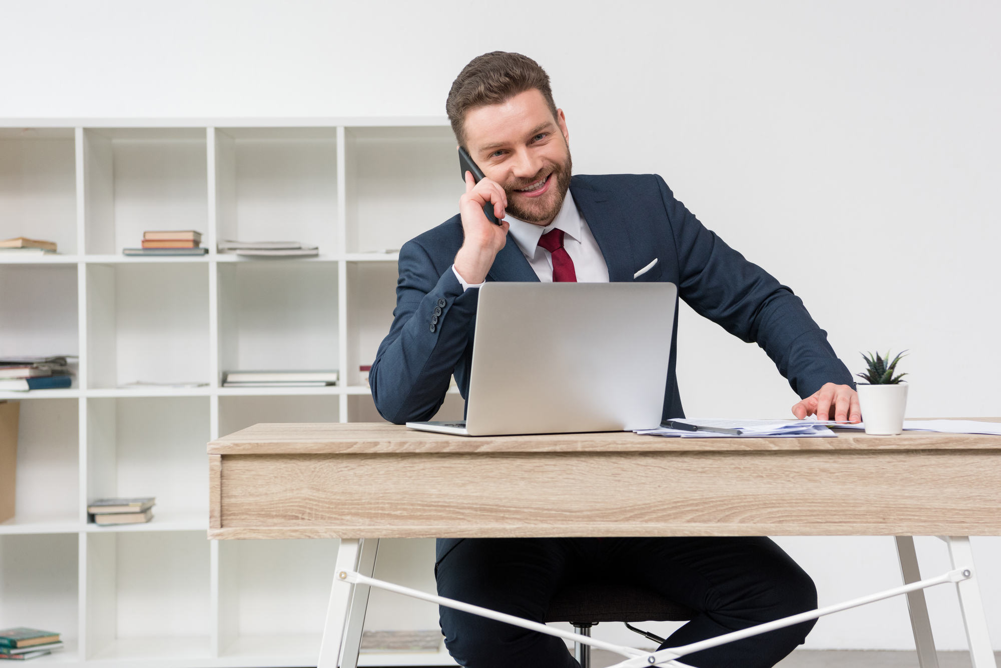 Hombre hablando por teléfono en una oficina sentado frente a un portatil situado en una mesa